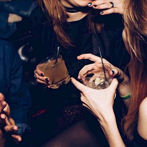 People are socializing, holding drinks, and enjoying a lively atmosphere, with smiles and gestures indicating a joyful moment.