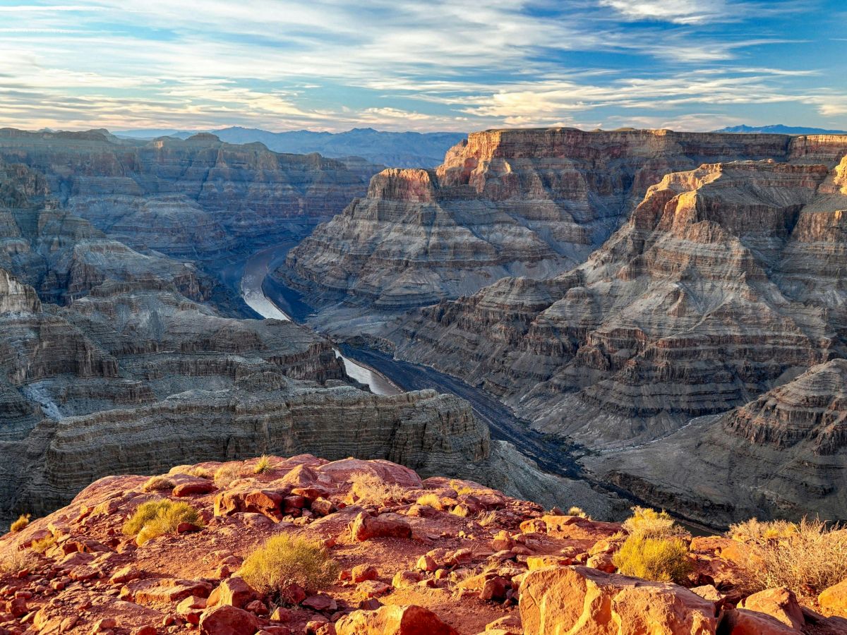 A breathtaking view of the Grand Canyon, showcasing its vast, colorful rock formations under a blue sky with scattered clouds.